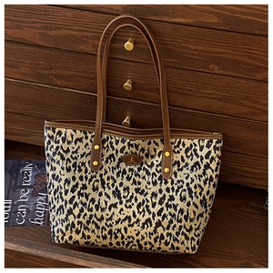 Detail of leopard print tote bag featuring brown leather handles and golden logo plate