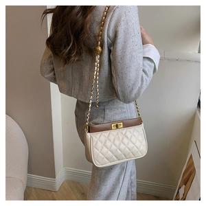 Detail of a quilted crossbody bag with gold chain strap worn by a model in gray outfit