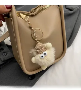 Detail of furry monster keychain with knit hat and big eyes on khaki bucket bag