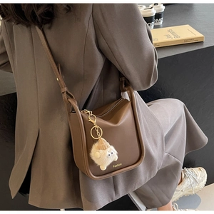 Detail of dark brown matte bucket bag with golden Fashion logo and a plush lamb charm