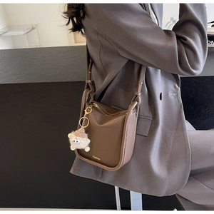 Detailed shot of brown leather bucket bag with gold Fashion logo and plush charm