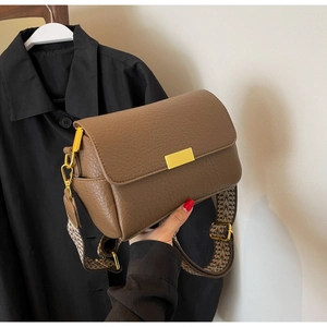 Close-up of brown litchi leather bag with gold buckle and wide woven shoulder strap