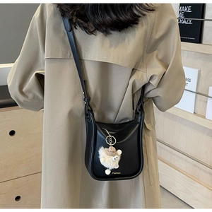 Close-up of black PU leather bucket bag with plush monster charm and Fashion text