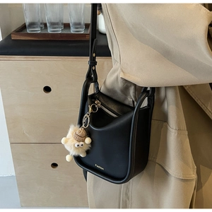 Detail of black leather bucket bag featuring a fuzzy monster charm and gold accents