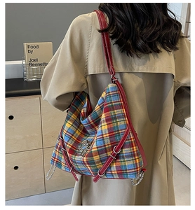 Detail of tartan tote bag with red leather strap and silver chain on trench coat