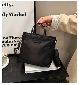 Détail d'un sac seau en nylon noir avec large bandoulière et boucles dorées