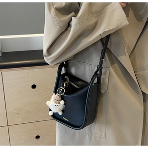 Detail view of black U-shaped shoulder bag with gold zipper and white plush monster charm