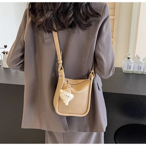 Detail showing beige leather bucket bag on model with white plush cartoon pendant charm
