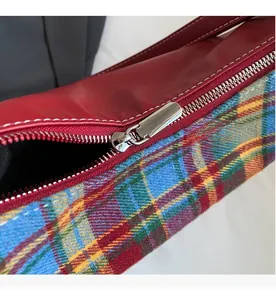 Detail of smooth silver zipper on burgundy leather and colorful plaid canvas bag