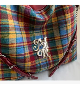 Close-up of colorful tartan tote bag with red leather trim and silver metal logo