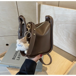 Detail of dark brown bucket bag with wide shoulder strap and white plush monster charm
