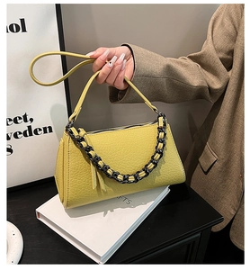 Detail of yellow-green crocodile embossed texture on a square bag with black chain strap
