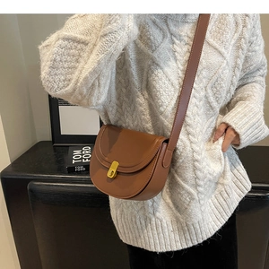 Close-up of a brown semi-circular saddle bag with golden metal twist lock on a white sweater