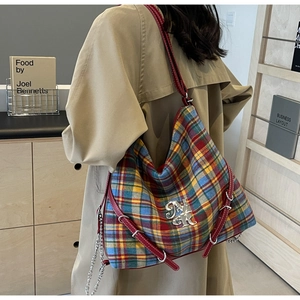Detail of red leather shoulder strap and metallic logo on tartan check tote bag