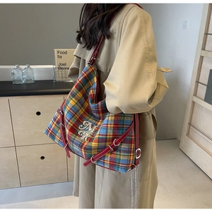 Detail of colorful plaid tote bag with red leather trim and silver metal logo