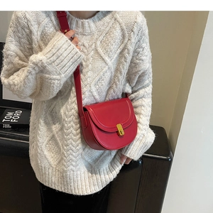 Detail of dark red leather saddle bag with golden clasp against a white knit sweater