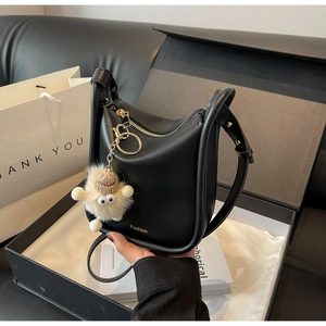 Detail of black leather hobo bag in a gift box with a cute plush monster charm