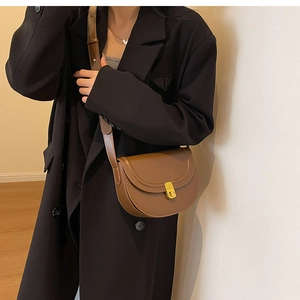 Close-up of brown faux leather saddle bag with gold metal clasp and visible stitching