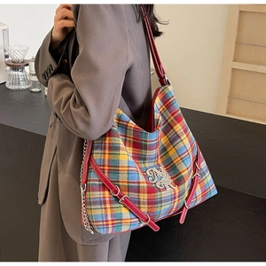Close-up of a large checkered canvas tote bag with red leather trim and metal chain detail