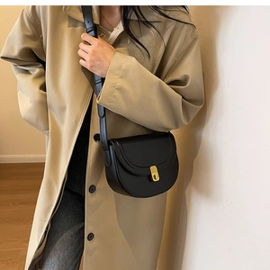 Detail of black semi-circular saddle bag with golden buckle on khaki trench coat