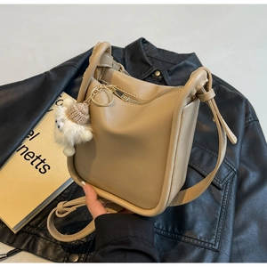 Detail of tan leather bucket bag with zipper and cute plush charm on a leather jacket