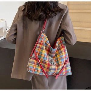 Detail of colorful plaid tote bag with red leather straps and silver metal chain accessory