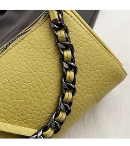 Detail of yellow pebbled leather handbag featuring bold dark metal chain strap with leather