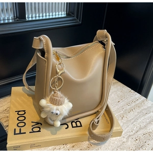 Detail of khaki bucket bag with plush charm on a book, vintage leather crossbody style