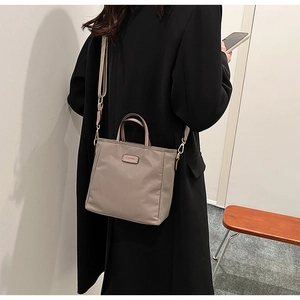 Detail of taupe waterproof nylon tote bag with adjustable strap worn with black coat
