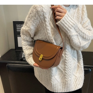 Detailed close-up of brown leather saddle bag with golden twist lock and smooth finish