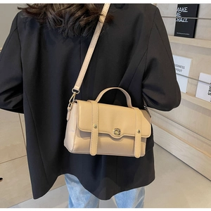 Sac carré beige chic porté sur un blazer noir montrant les détails de la bandoulière