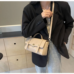 Détail du sac bandoulière beige en similicuir avec fermoir rotatif doré sur la tenue