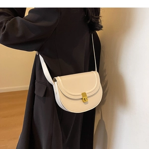 Side view of a beige minimalist saddle bag with a gold buckle worn as a crossbody purse