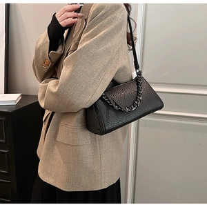 Detail of black litchi texture crossbody bag with metal chain and slim shoulder strap