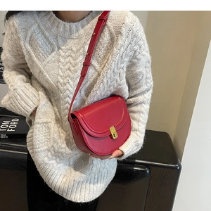 Detailed view of red leather saddle bag with gold metal buckle worn with cream sweater