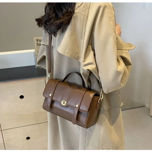 Sac bandoulière en cuir marron avec poignée et boucle dorée porté avec un trench beige