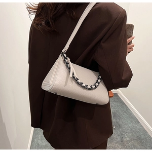 Detail of off-white crocodile texture shoulder bag with decorative acrylic chain on model