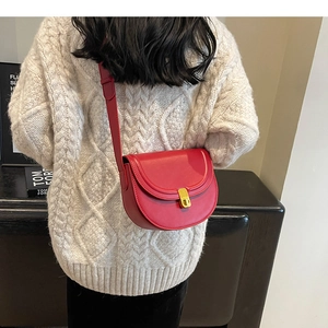 Detail of red leather saddle bag with gold metal clasp on beige knit sweater background