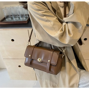 Détail d'un sac bandoulière vintage marron avec un fermoir rotatif en métal doré