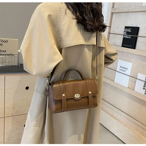 Détail d'un sac à main vintage en cuir marron avec fermoir doré sur un trench-coat