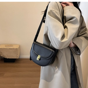Detail of a black leather saddle bag featuring a gold buckle on a model in a trench coat