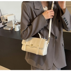 Sac bandoulière crème chic avec fermoir doré présenté dans un décor de café
