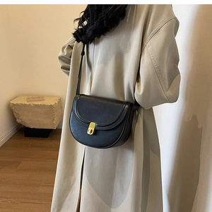 Detail of minimalist black leather saddle bag with gold metal clasp on a beige coat