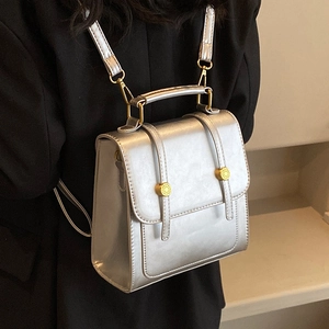 Silver metallic leather backpack with gold buckles shown on a model in a minimal setting