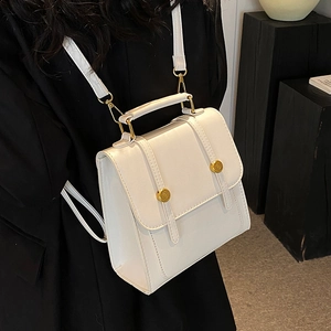 Minimalist white structured backpack with gold hardware worn over a black blazer