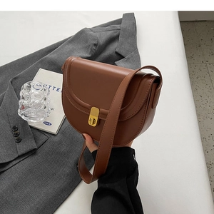 Detail of a brown leather saddle bag with vintage gold buckle held against a grey suit