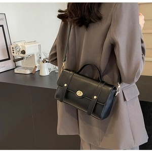 Détail d'un sac bandoulière vintage en cuir noir avec boucle dorée porté par un mannequin