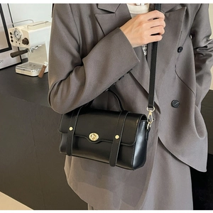 Détail du sac bandoulière en similicuir noir avec fermoir doré et brides verticales
