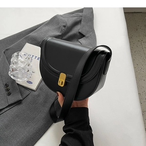 Detail of a matte black saddle bag featuring a vertical golden metal clasp and wide strap