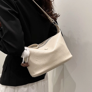 Chic beige bucket bag with soft pleated texture and plush charm, shown on model
